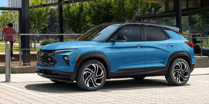 Blue compact SUV parked outside a modern glass-front building, shown from the side with large alloy wheels and landscaped greenery in the background