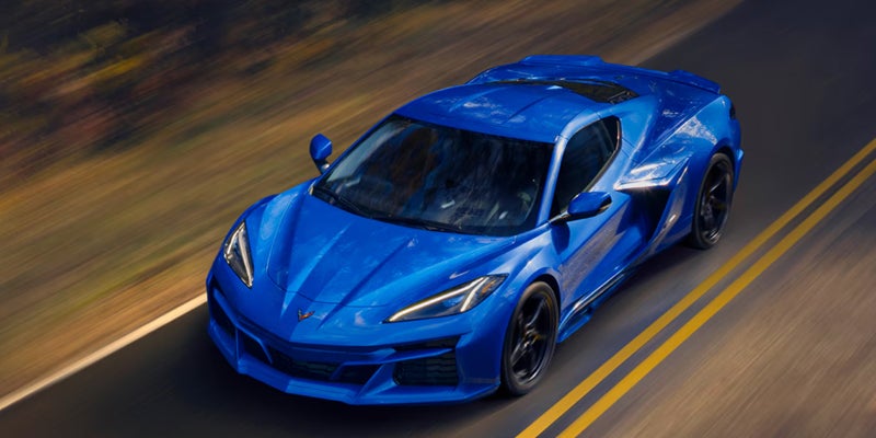 Blue sports car driving on a two-lane road, photographed from above with motion blur in the surrounding landscape