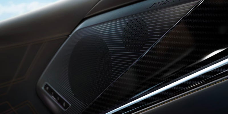Close-up of a premium car door speaker integrated into a dark carbon-fiber interior panel with metallic trim