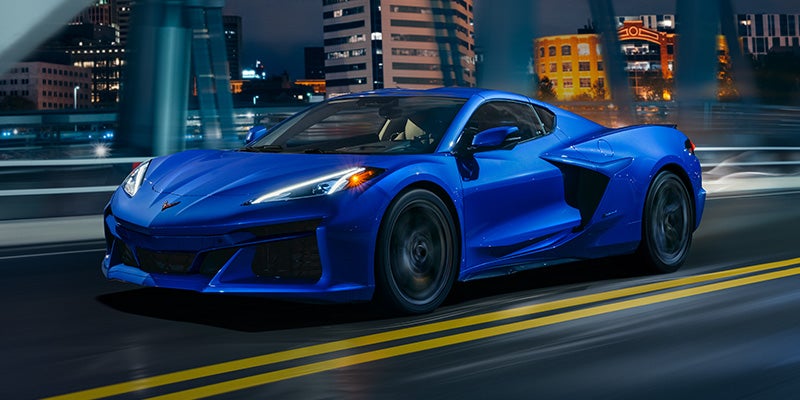 Blue sports car driving through a city at night, with illuminated buildings and motion blur emphasizing speed