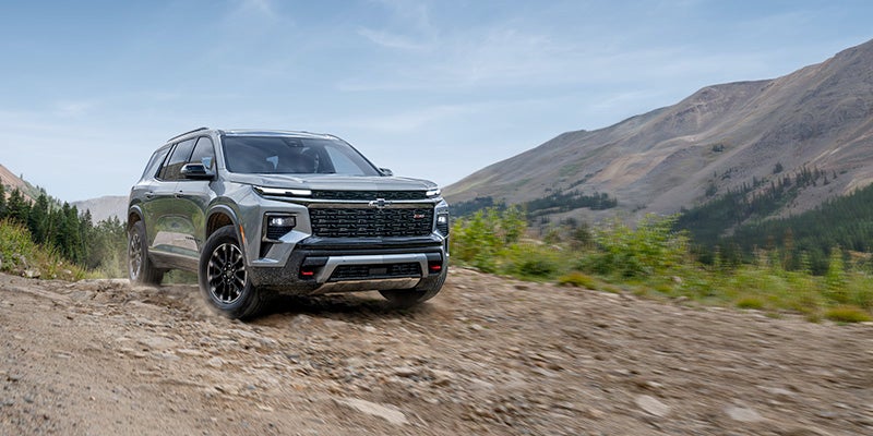 Black SUV driving along a rocky mountain trail, with dust rising from the tires and rugged hills in the background