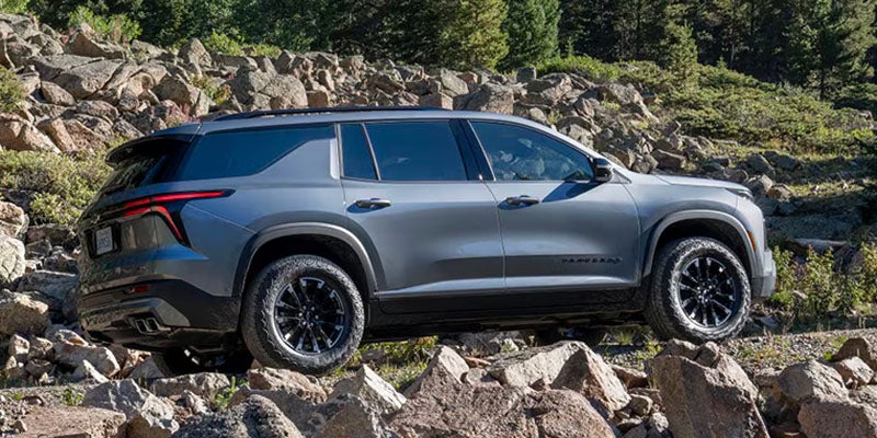 Gray SUV navigating a rocky off-road terrain, shown in side profile with large boulders and evergreen trees surrounding the vehicle