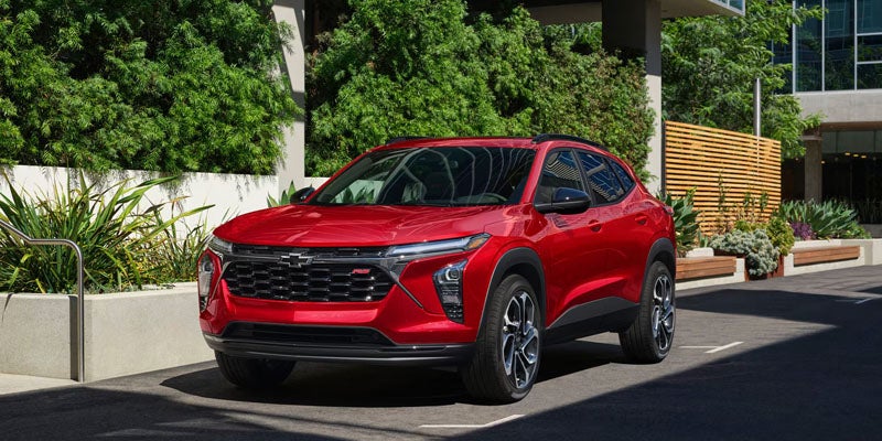 Red compact SUV driving on a city street, surrounded by landscaped greenery and modern buildings
