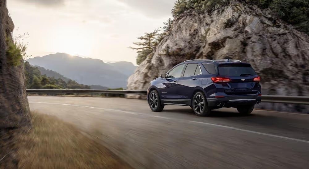 One of the most popular Chevy lease deals, a dark blue 2022 Chevy Equinox, is shown driving past a rock face.