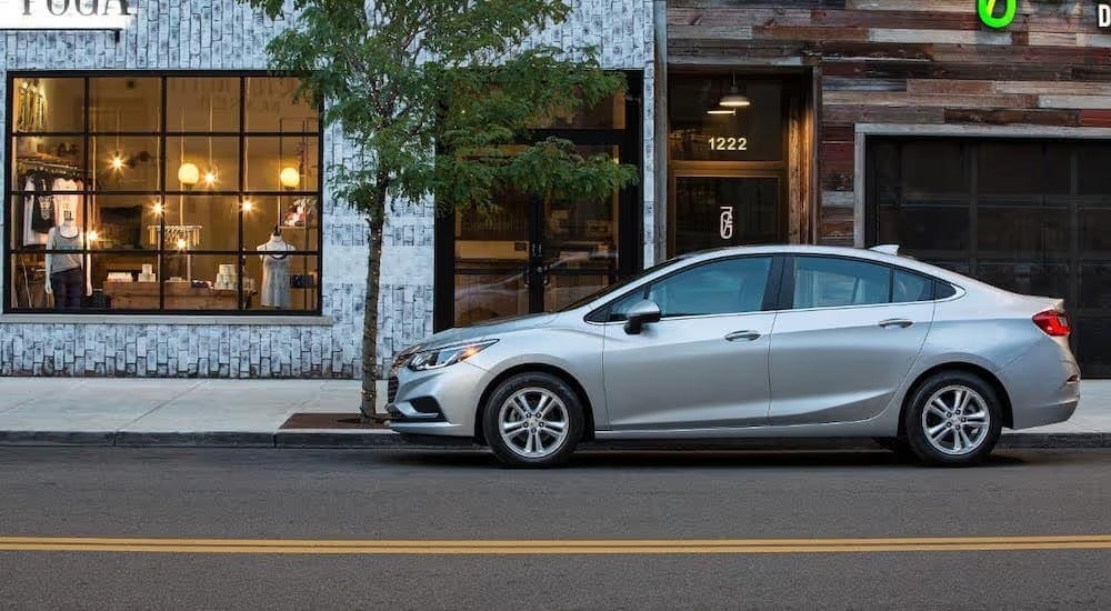 A silver 2016 Chevy Cruze sedan is shown from the side parked in front of a shop.