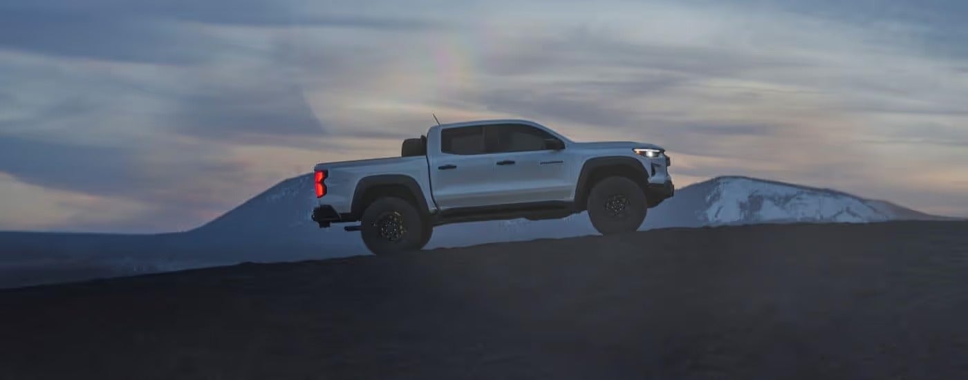 A white 2024 Chevy Colorado ZR2 Bison is shown driving past a mountain after leaving a Quakertown Chevy dealer.