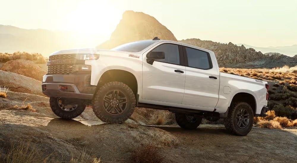 A white lifted Chevy Silverado 1500 Trailboss, which is a popular model among new lifted trucks in Bethlehem, PA, is rock crawling at sunset.
