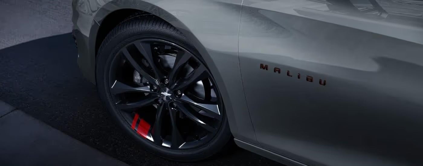 A close up shows the black and red wheel on a grey 2023 Chevy Malibu Redline.