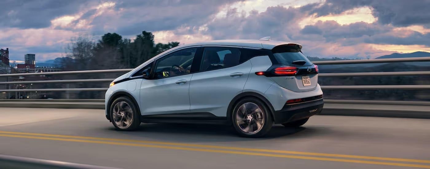 A light blue 2022 Chevy Bolt EV is driving on a highway at sunset.