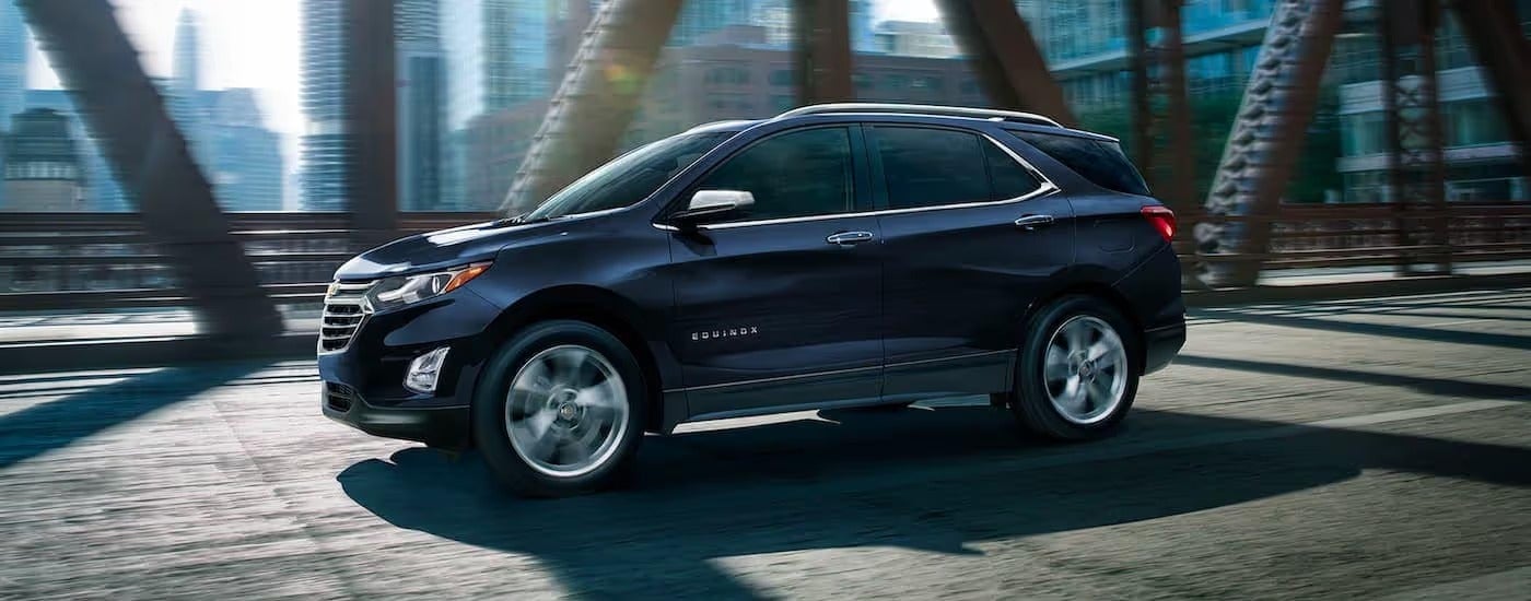 A blue 2021 Chevy Equinox is shown driving over a bridge in the city.