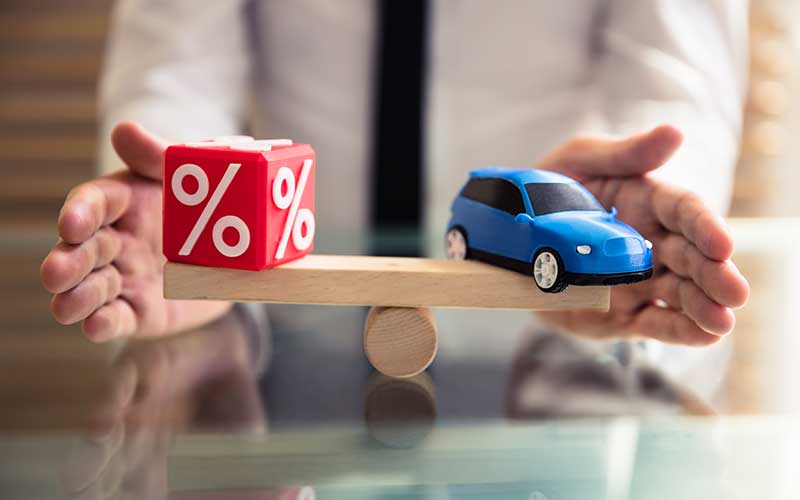 Model car and percentage symbol block balanced on a wooden seesaw, representing vehicle financing or interest rates